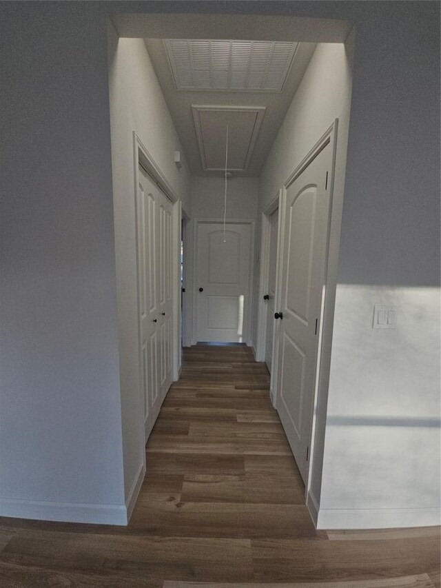 hall featuring attic access, wood finished floors, baseboards, and visible vents