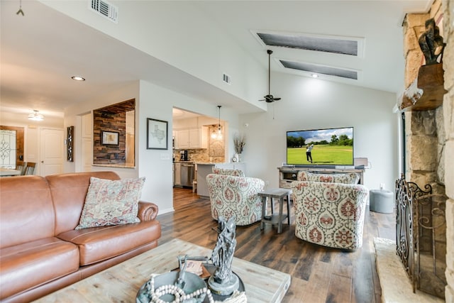 living area featuring a ceiling fan, wood finished floors, visible vents, vaulted ceiling, and a large fireplace