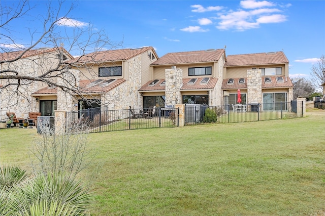 back of house with a tile roof, a lawn, stone siding, and a fenced backyard