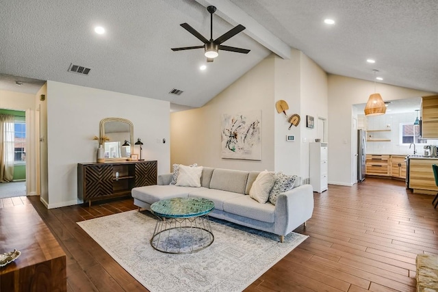 living area featuring visible vents, a textured ceiling, vaulted ceiling with beams, and dark wood-style flooring