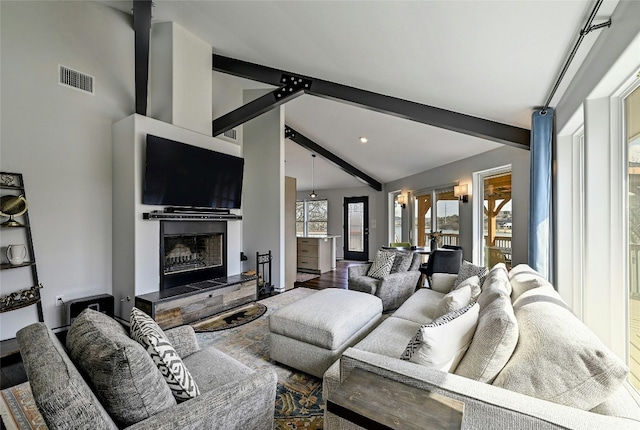 living room with beamed ceiling, a fireplace with raised hearth, visible vents, and a wealth of natural light