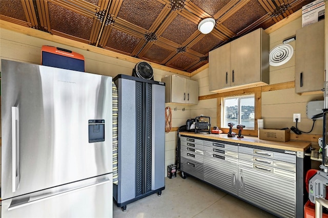 kitchen with an ornate ceiling, light countertops, concrete flooring, wood walls, and stainless steel fridge