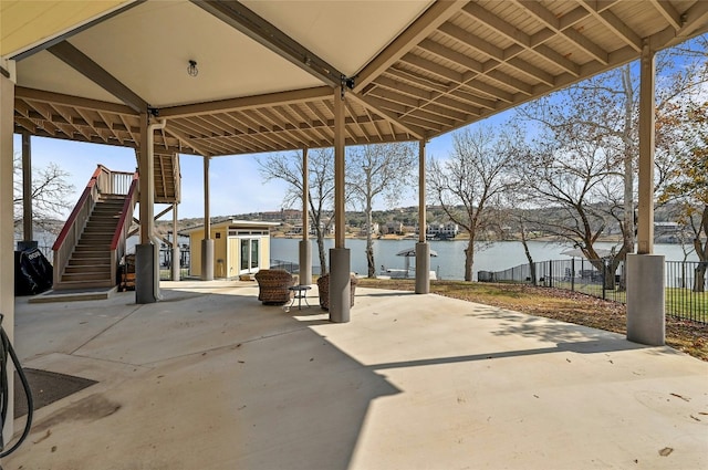 view of patio featuring stairway, a water view, and fence