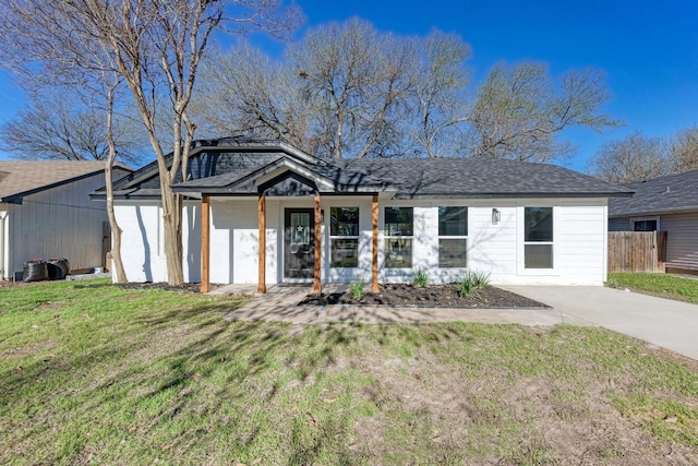 view of front facade featuring a shingled roof, a front lawn, and fence