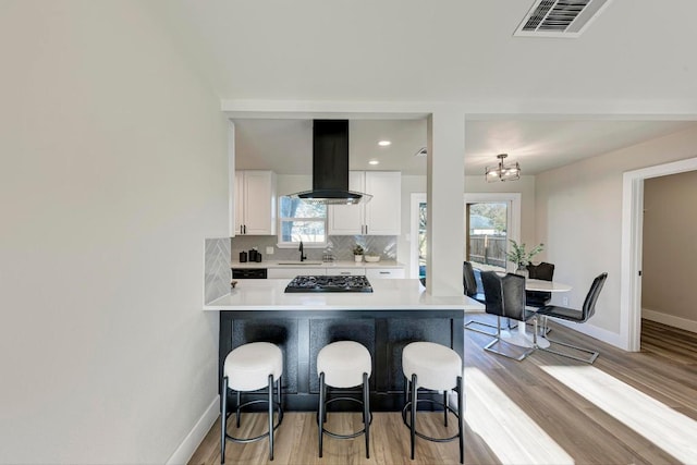 kitchen with visible vents, a kitchen bar, a sink, tasteful backsplash, and exhaust hood