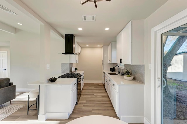 kitchen featuring visible vents, a sink, light countertops, black range with gas stovetop, and wall chimney range hood