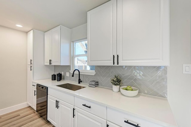 kitchen with backsplash, dishwasher, white cabinetry, and a sink