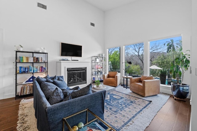 living room with a glass covered fireplace, a high ceiling, visible vents, and wood finished floors