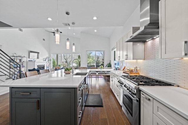 kitchen with high end stove, wall chimney range hood, a fireplace, light countertops, and dark wood-style flooring