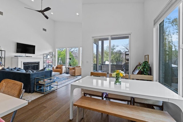 dining room featuring visible vents, recessed lighting, a high ceiling, wood finished floors, and a glass covered fireplace