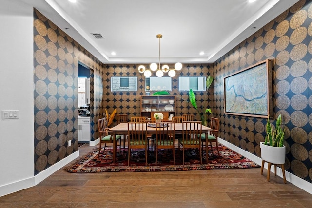 dining room featuring wood finished floors, baseboards, visible vents, wallpapered walls, and a chandelier