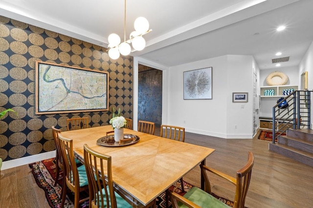 dining space with wallpapered walls, an accent wall, baseboards, and wood finished floors