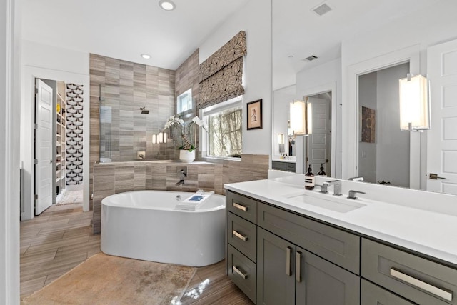 bathroom featuring vanity, visible vents, a tile shower, a freestanding bath, and tile walls