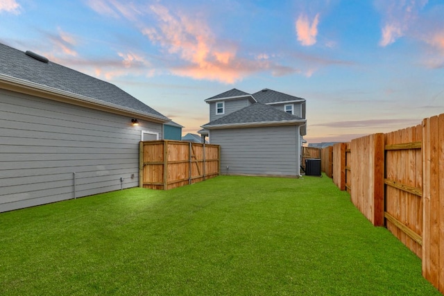 yard at dusk with cooling unit and a fenced backyard