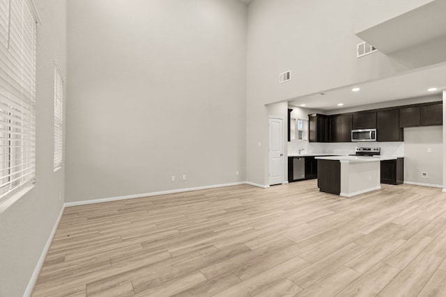 unfurnished living room with light wood finished floors, visible vents, a high ceiling, and baseboards