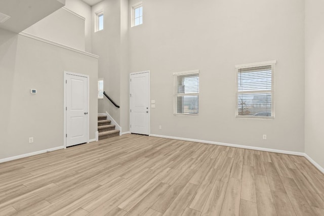 unfurnished living room featuring stairway, light wood-style flooring, plenty of natural light, and baseboards