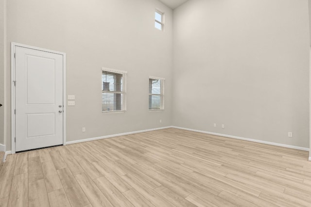 unfurnished room with a high ceiling, light wood-type flooring, and baseboards