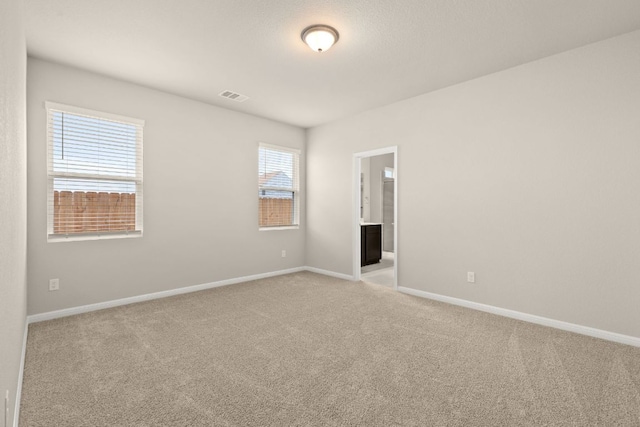 spare room featuring light carpet, visible vents, and baseboards