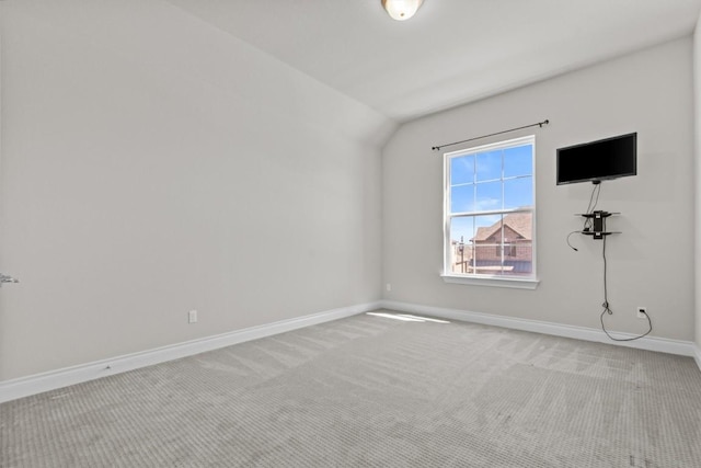 carpeted empty room with baseboards and vaulted ceiling