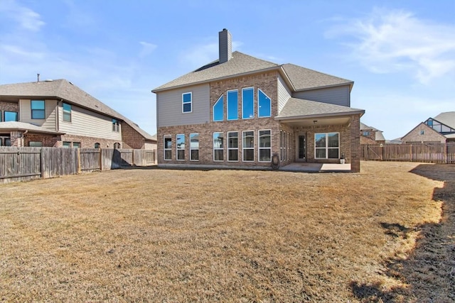 rear view of property featuring a yard, a fenced backyard, brick siding, and a chimney