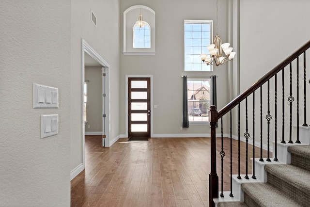 foyer entrance with visible vents, a notable chandelier, wood finished floors, baseboards, and a towering ceiling