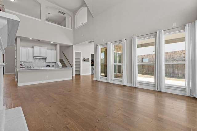 unfurnished living room featuring visible vents, wood finished floors, recessed lighting, stairway, and baseboards