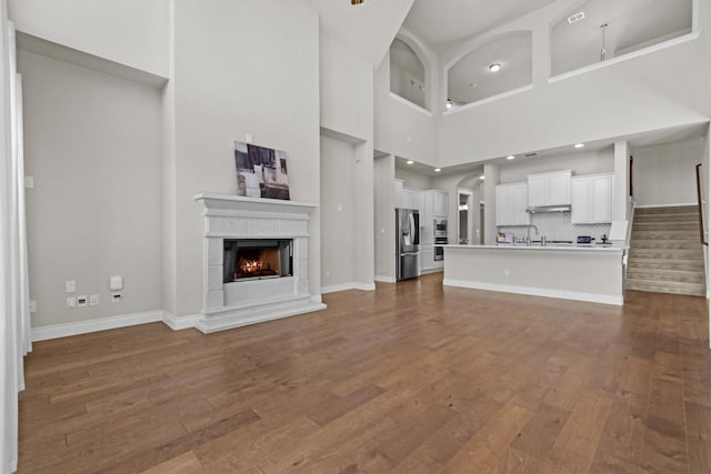 unfurnished living room with dark wood-style floors, baseboards, stairs, and a lit fireplace