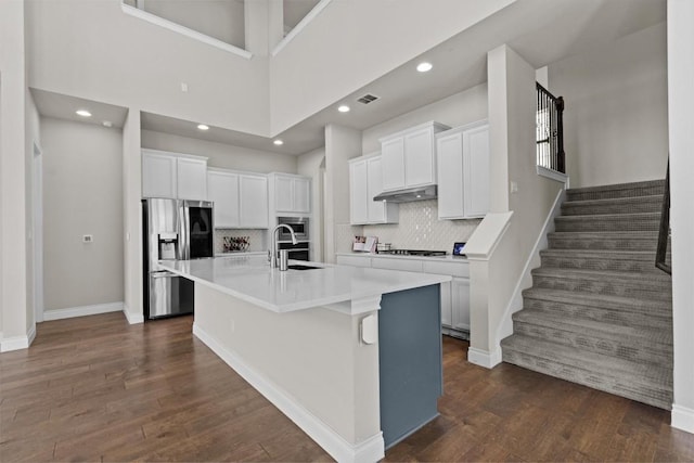 kitchen featuring dark wood-type flooring, an island with sink, under cabinet range hood, a sink, and stainless steel appliances