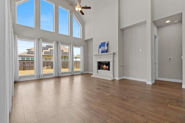 unfurnished living room featuring ceiling fan, a warm lit fireplace, baseboards, and wood finished floors