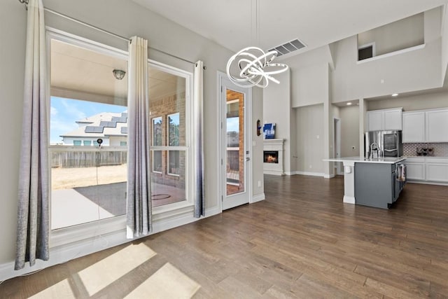 unfurnished dining area featuring a lit fireplace, visible vents, an inviting chandelier, and dark wood-style flooring