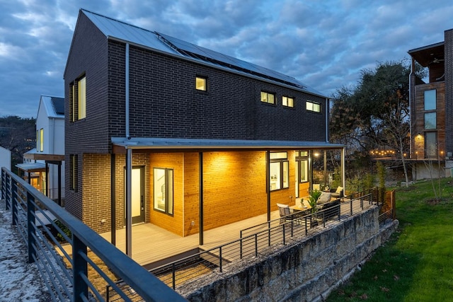 back of property with brick siding, solar panels, and fence