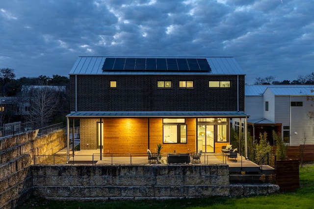 back of house with metal roof, roof mounted solar panels, central AC unit, and a standing seam roof