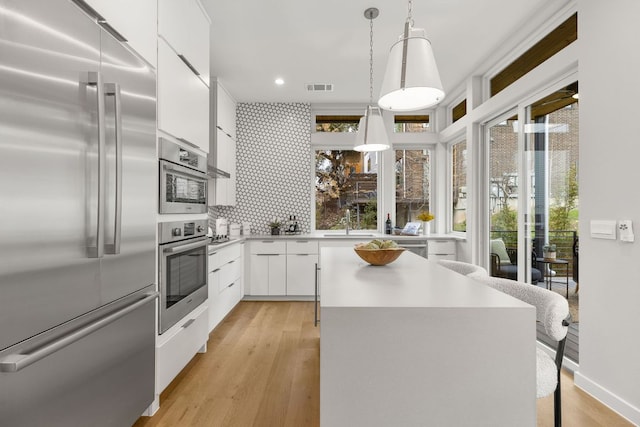 kitchen featuring a kitchen island, light wood-style flooring, stainless steel appliances, white cabinetry, and modern cabinets