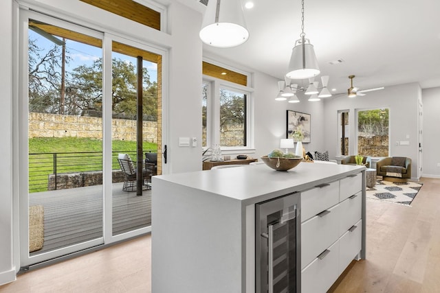 kitchen featuring beverage cooler, open floor plan, pendant lighting, light wood-style floors, and white cabinets