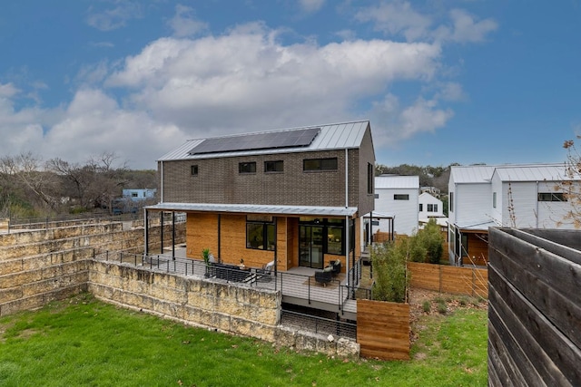 back of property featuring a standing seam roof, roof mounted solar panels, a fenced backyard, a yard, and metal roof