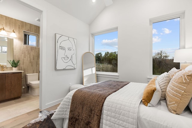 bedroom featuring vaulted ceiling, light wood-style flooring, multiple windows, and ensuite bathroom