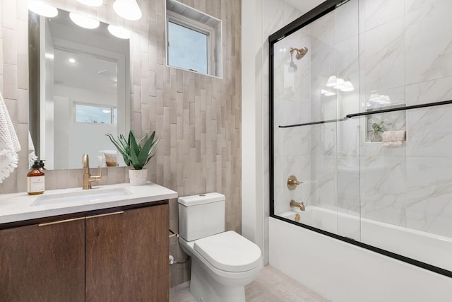 full bath featuring bath / shower combo with glass door, toilet, tile walls, and vanity