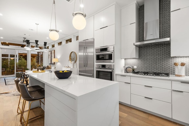 kitchen featuring wall chimney range hood, modern cabinets, appliances with stainless steel finishes, and a kitchen island