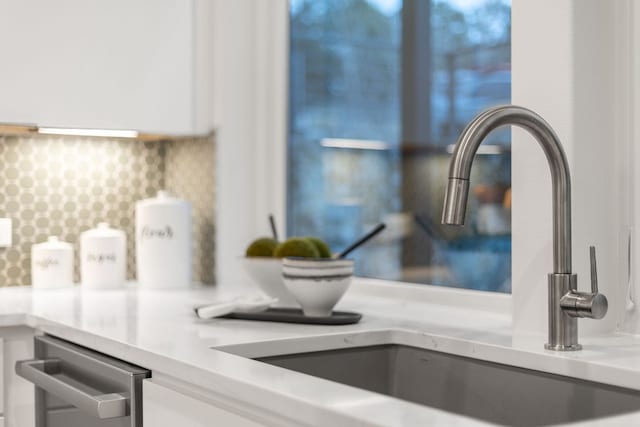 room details with backsplash, white cabinets, light countertops, and a sink