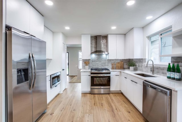 kitchen with a sink, wall chimney range hood, light countertops, stainless steel appliances, and modern cabinets