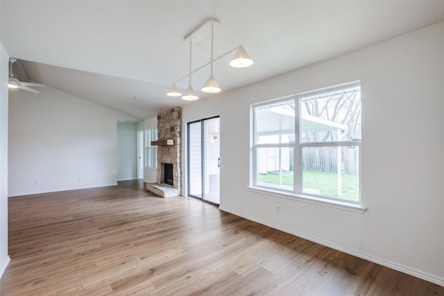 unfurnished living room featuring baseboards, vaulted ceiling, a stone fireplace, wood finished floors, and a ceiling fan