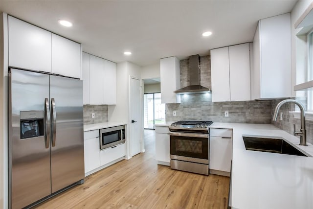 kitchen with modern cabinets, a sink, appliances with stainless steel finishes, wall chimney exhaust hood, and light countertops