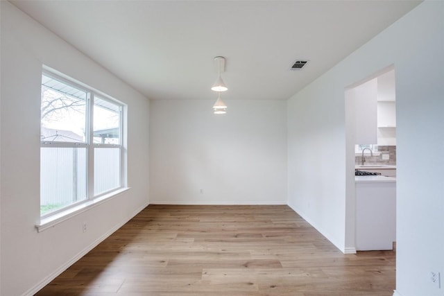 spare room featuring a sink, light wood-style floors, visible vents, and baseboards