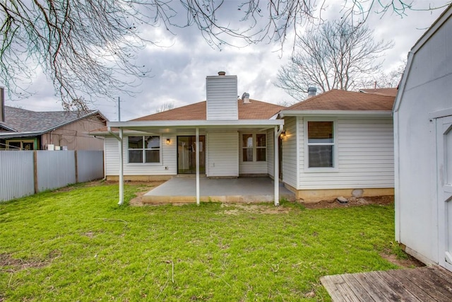 rear view of property with a patio, a lawn, a chimney, and fence