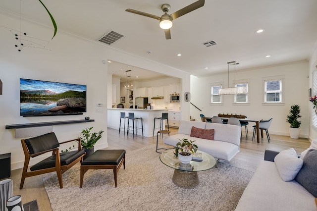 living room with crown molding, light wood-style flooring, and visible vents