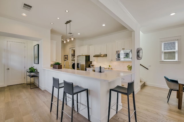 kitchen featuring a kitchen breakfast bar, visible vents, under cabinet range hood, and stainless steel appliances