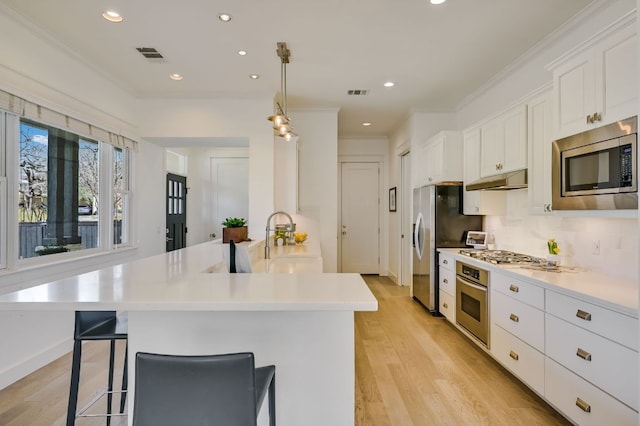 kitchen featuring light wood finished floors, stainless steel appliances, under cabinet range hood, white cabinetry, and crown molding