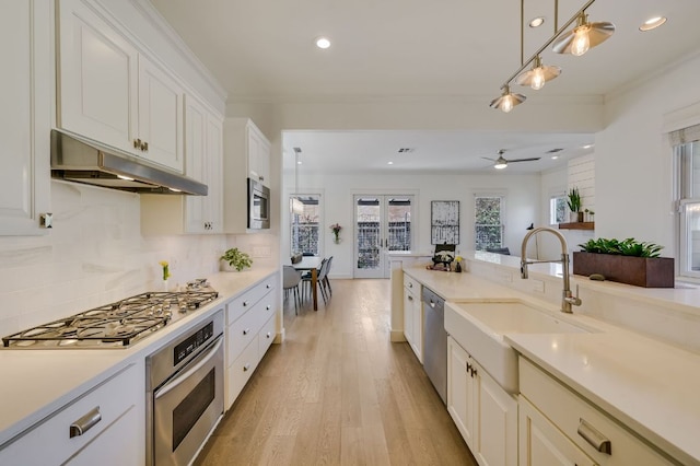 kitchen with under cabinet range hood, a sink, backsplash, appliances with stainless steel finishes, and light countertops