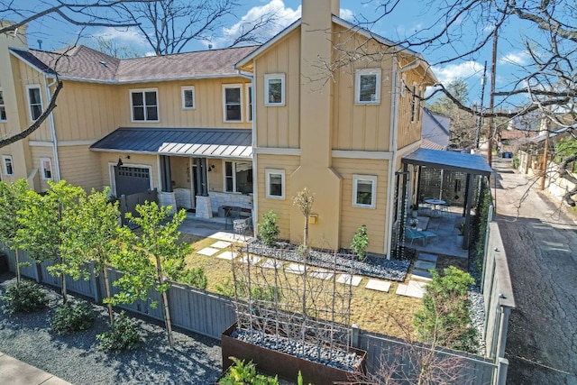 view of front facade with fence, a standing seam roof, covered porch, a chimney, and board and batten siding