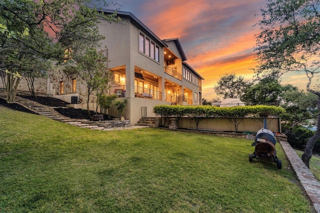 back of house at dusk featuring a lawn and stucco siding